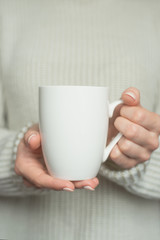 Obraz na płótnie Canvas Girl in warm sweater is holding white mug in hands.. Mockup for winter gifts design.