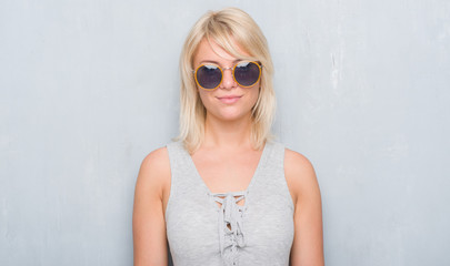 Adult caucasian woman over grunge grey wall wearing retro sunglasses with a confident expression on smart face thinking serious