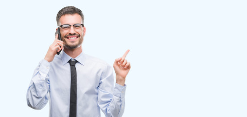 Young business adult man talking on the phone very happy pointing with hand and finger to the side