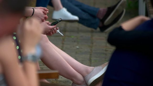 Woman with cigarette and smartphone. Close up. Smoking in crowded area.