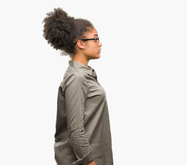 Young afro american woman wearing glasses over isolated background looking to side, relax profile pose with natural face with confident smile.