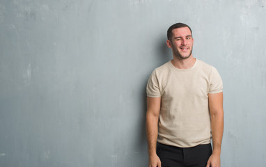 Young caucasian man over grey grunge wall winking looking at the camera with sexy expression,...