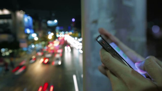 woman use smartphone touch screen texting chat close up shot urban night traffic vehicle light trail long exposure time lapse fast speed in the background