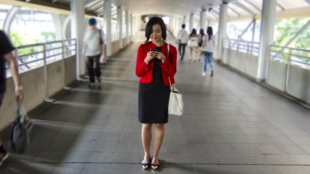 Asian Chinese business woman in casual cloth happy using a smartphone with smiling face while walking in urban pedestrian walkway of financial district hyperlapse shot