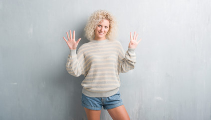 Young blonde woman with curly hair over grunge grey background showing and pointing up with fingers...