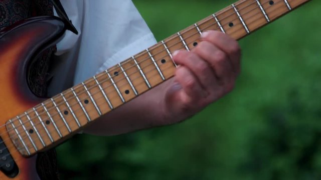 Mature male hands playing guitar outdoors. Close up. Old wooden guitar.