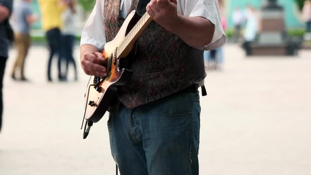Adult man playing guitar outdoor in the park. Crowded area. Unrecognizable.