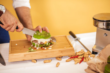 Man cuttung fresh self made juicy burger with green bun on wooden plate, close up