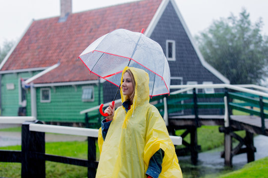 Young girl in rain suit with umbrella stay on bridge with dutch house on background. Netherlands