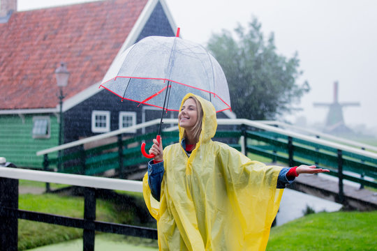 Young girl in rain suit with umbrella stay on bridge with dutch house on background. Netherlands