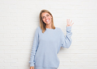 Beautiful young woman over white brick wall showing and pointing up with fingers number four while smiling confident and happy.