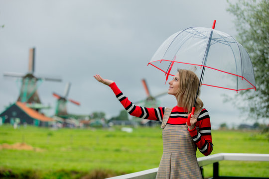 Young girl in dress with umbrella stay on bridge with dutch mills on background. Netherlands
