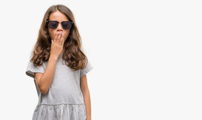 Brunette hispanic girl wearing sunglasses bored yawning tired covering mouth with hand. Restless and sleepiness.