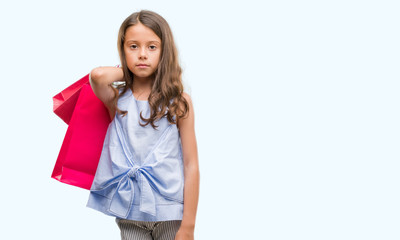 Brunette hispanic girl holding shopping bags with a confident expression on smart face thinking serious
