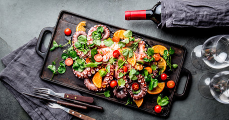 Whole octopus salad with orange, tomatoes and cress salad served on board with wine