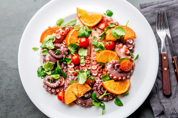 Whole octopus salad with orange, tomatoes and cress salad on white plate. Top view © lblinova