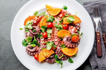 Whole octopus salad with orange, tomatoes and cress salad on white plate. Top view