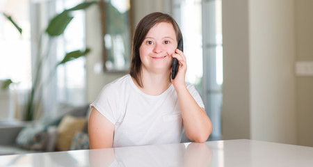 Down syndrome woman at home using smartphone with a happy face standing and smiling with a...