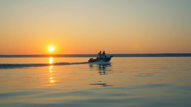 Fishing autoboat is slowly sailing across water with two men in it