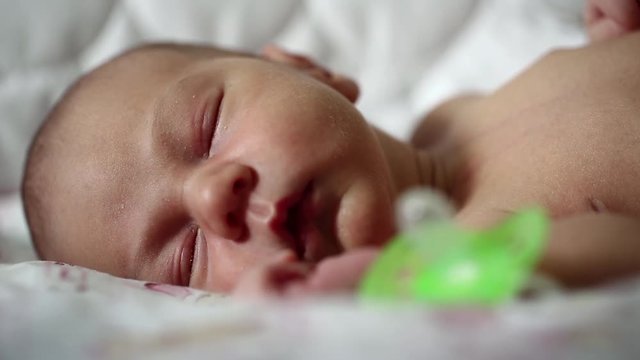 Newborn baby sleeps. Newborn 2 weeks old baby boy lies on the bed and sleeps. Green pacifier lies is near