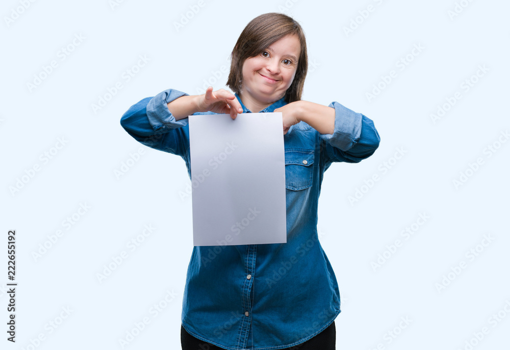 Sticker young adult woman with down syndrome holding blank paper sheet over isolated background with surpris