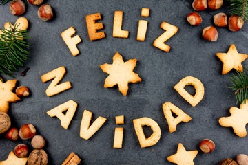 FELIZ NAVIDAD COOKIES. Words Merry Christmas en Spanish with baked cookies, Christmas decoration and nuts on black slate background. Christmas card for hispanic countries top view