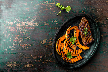 Grilled meat and pumpkin on black plate. Autumn menu. Top view