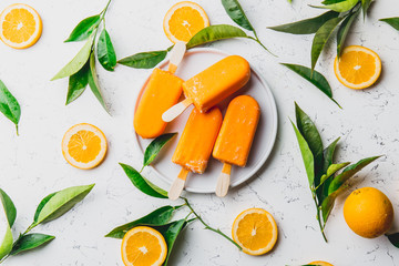 Homemade orange ice cream on stick. white background with orange fruits slices and orange tree leaves. Orange popsicles lollipop