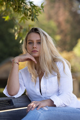 young blonde teenager sitting a on bench in the shade
