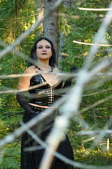A woman of a witch in black stands in dense forest thickets. Halloween.