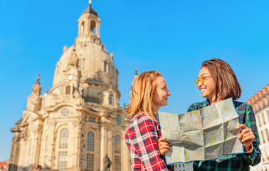 Two happy women hugging and looking at the map near main attraction of Dresden - Frauenkirche . The concept of love and friendship in travel