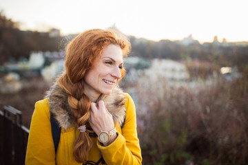 Red hair beautiful woman wearing yellow coat walking outdoors. Autumn time, city on background