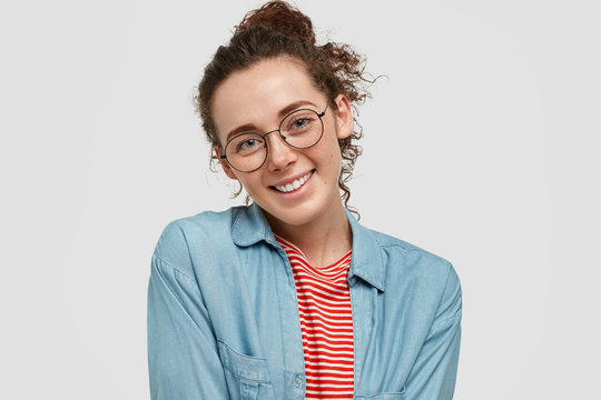 Horizontal shot of pleased student with freckled skin, glad to see results of her work, wears spectacles, dressed in casual clothes, isolated on white background. People, lifestyle, positive emotions