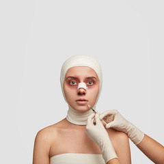 Vertical shot of young female patient undergoes plastic surgery of nose, has medical bandages on...