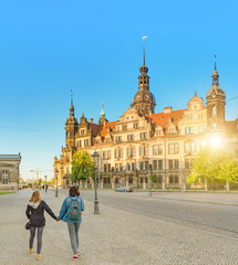 Obraz premium Friends holding hand in hand and walking near the Dresden Castle with Hausmannsturm Tower at sunset