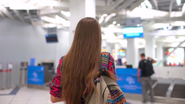 Young travel woman in casual shirt with the baggage walking in the modern airport terminal. View from the back. city airport travel tourism baggage departure destination business. slow-motion
