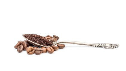 Metal spoon with ground coffee on pile of coffee beans.