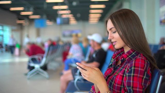 Woman using smartphone in the airport. Traveler girl waiting in airport and using her smart phone. Pretty young female passenger at the airport. city airport travel tourism baggage technologies