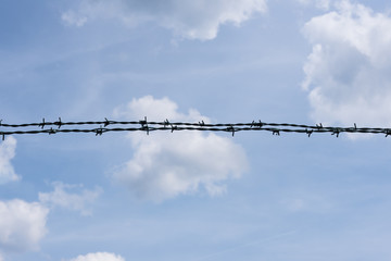 Barbed wire against cloudy blue sky - isolated design element