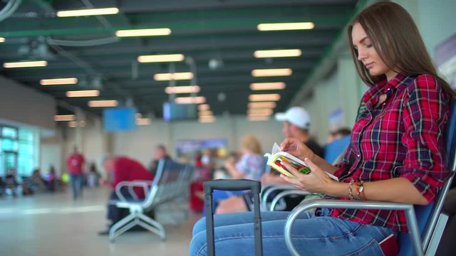 Airport waiting for a flight. Pretty young female passenger at the airport. Female traveler waiting for departure and reading book. slow-motion