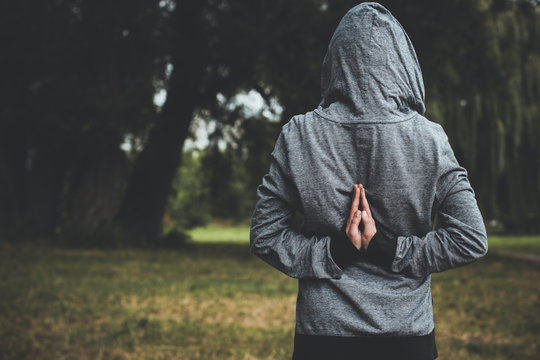 creative prayer pose by human hands concept shot with backwards clothes gray hoodie on body and face behind hood on natural unfocused bokeh effect background and empty copy space for your text
