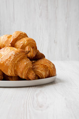 Freshly baked croissants on grey round plate on white wooden surface, side view.