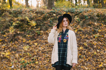 Stylish hippie girl in a knitted sweater and hat walks in the autumn park.