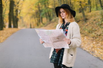 Hippie girl with a map, old camera in a knitted sweater and hat walks autumn park.