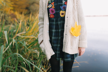 Hippie girl with a yellow maple leaf in a knitted sweater and hat walks autumn park.