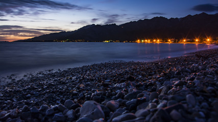 Evening landscape after sunset. City of lights and illuminated stones on the beach. Sea water like fog.