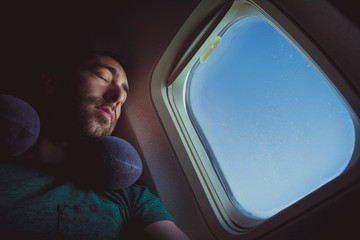 Young man with neck pillow resting and sleeping on an airplane