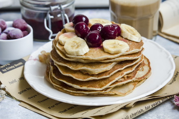 Pancakes with banana and cherries on the top and a cup of coffee