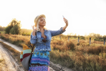 Young millennial blonde Caucasian woman taking a selfie on digital camera in park in autumn. Cool teenage girl photographing herself using digital camera. Matte filter, natural light.