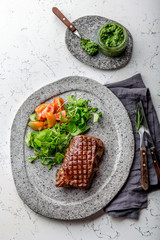 Grilled beef steak tenderloin on gray stone plate with salad and chimichurri sauce